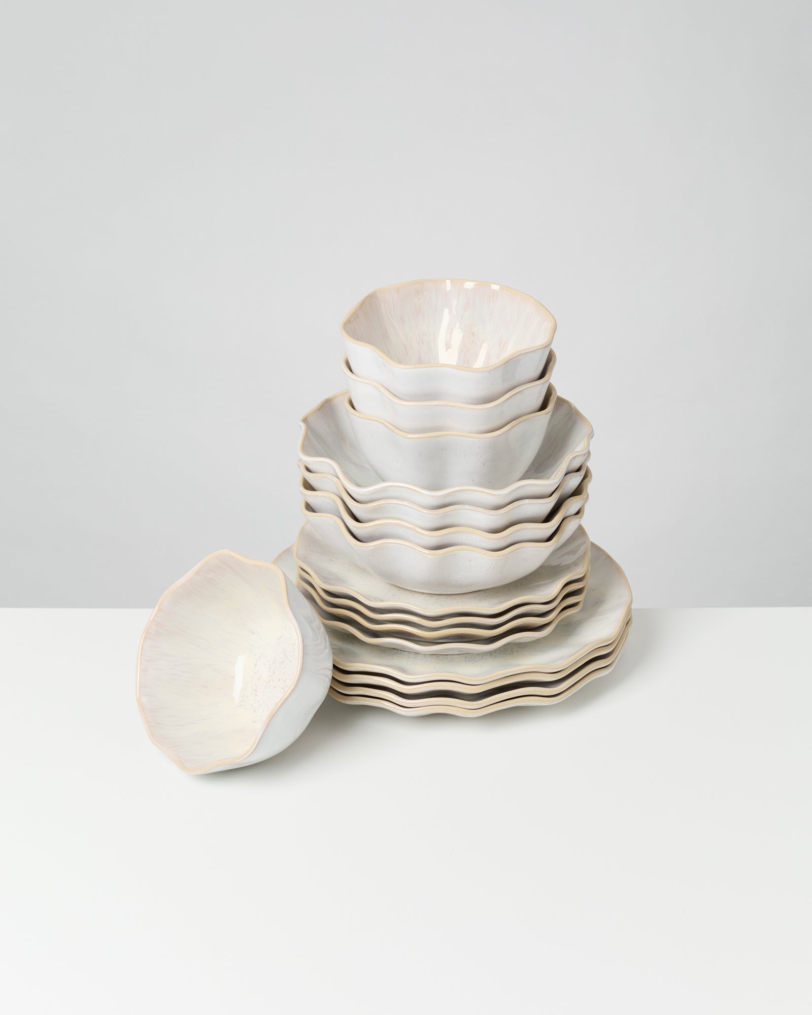 Ein Stapel wellenförmiger, weißer Keramikteller und -schüsseln auf einem weißen Tisch.