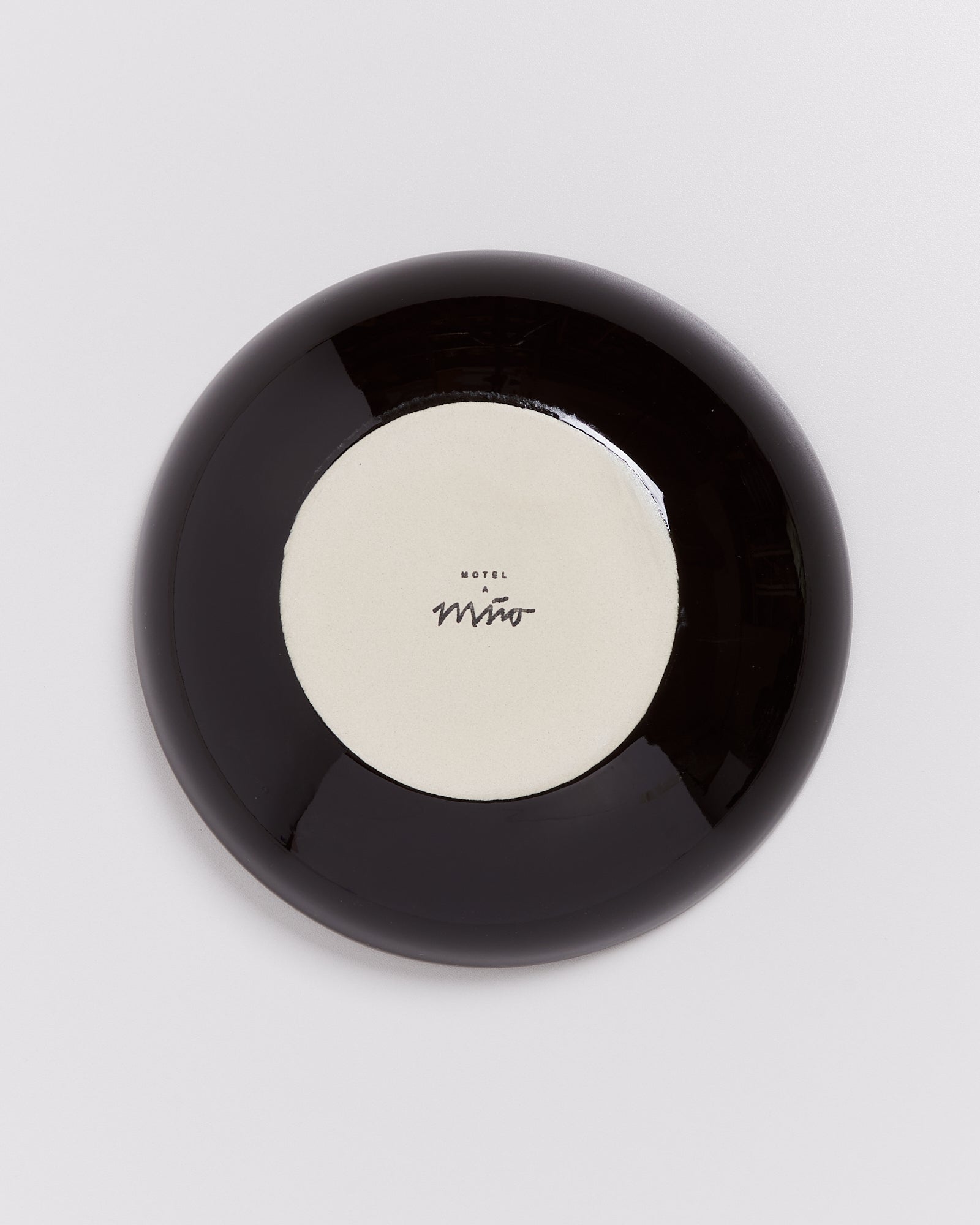Schwarzer Teller mit cremefarbener Mitte und der Aufschrift "Motel a Miio" in der Mitte.