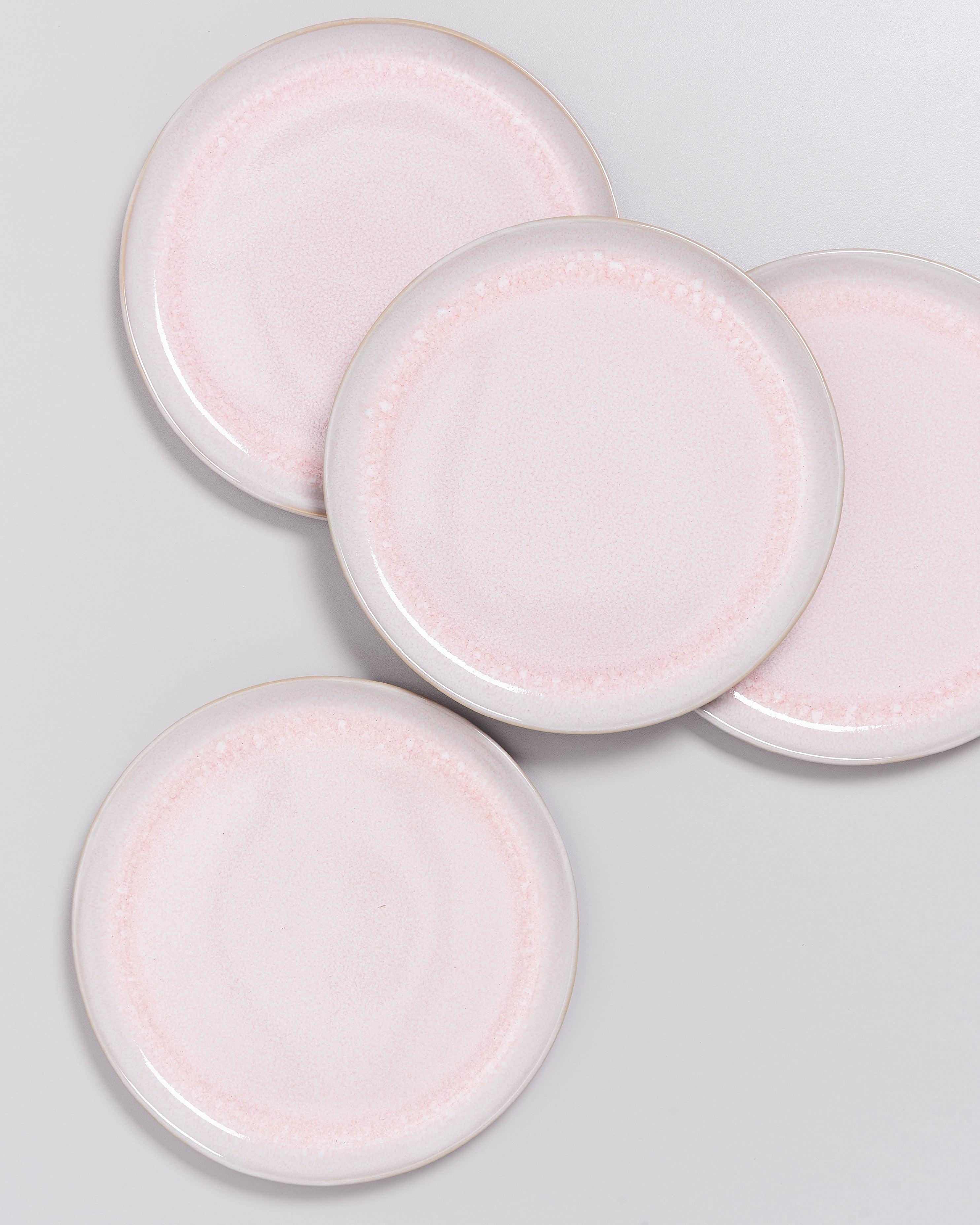 Vier rosa Keramikteller auf weißem Hintergrund in leicht überlappender Anordnung.