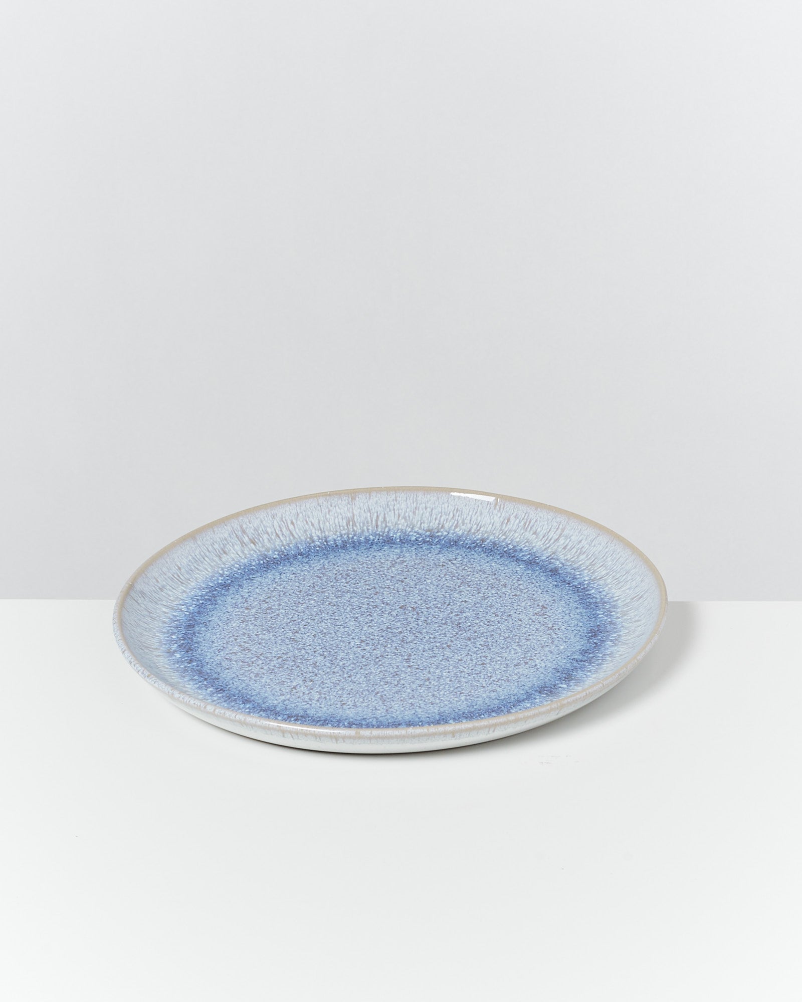 Ein blauer Keramikteller mit gesprenkeltem Muster steht auf einem weißen Tisch vor einem grauen Hintergrund.